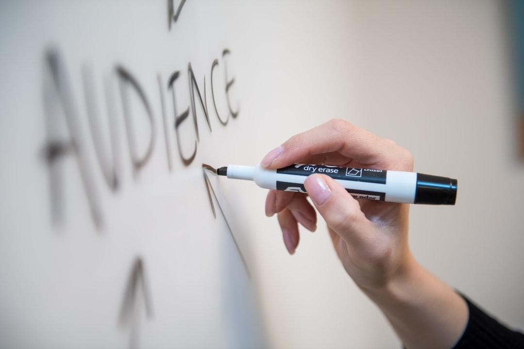 A woman’s hand writes the word audience on a whiteboard, with arrows.